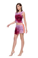 Three-quarter front view of the Marea Sunset Gradient wetlook skirt set, showing curved folds and peach detailing at the hip.