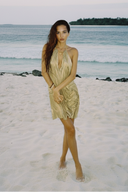 Full-length beach view of the metallic gold Silver Moon halter dress with a draped asymmetric skirt.